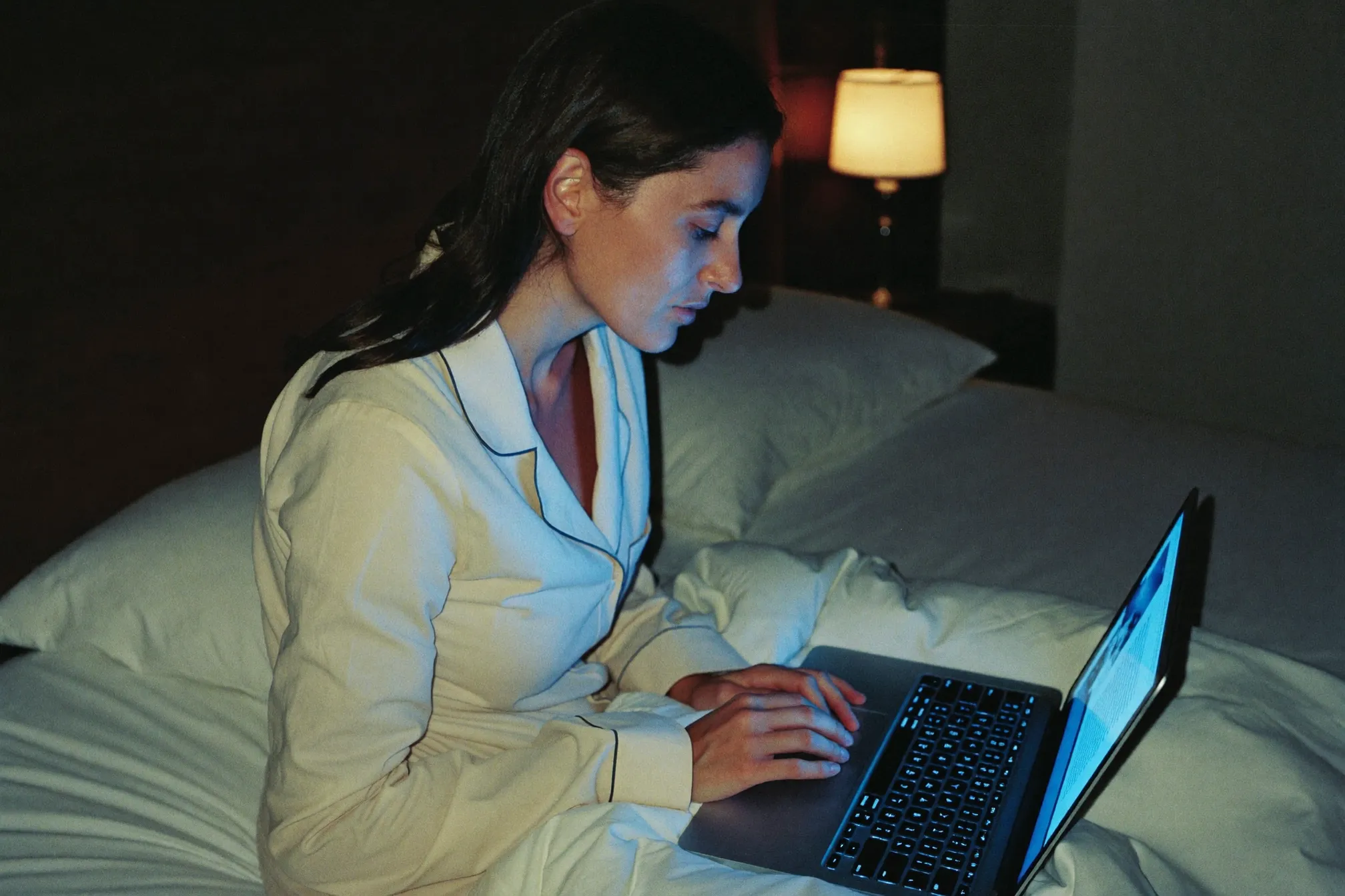 Donna in pigiama che legge il laptop di notte, espressione di scoperta concentrata.