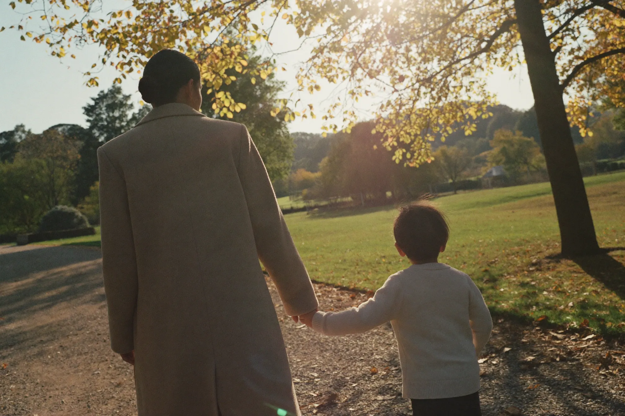 Madre e figlio che camminano mano nella mano in un parco alla luce dorata del tramonto.